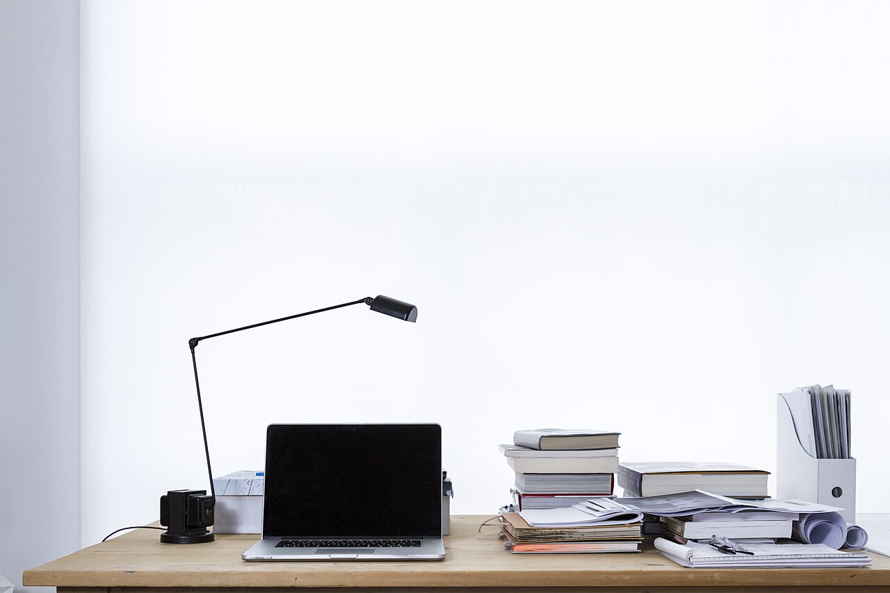 A laptop on a tidy desk beside a stack of books
